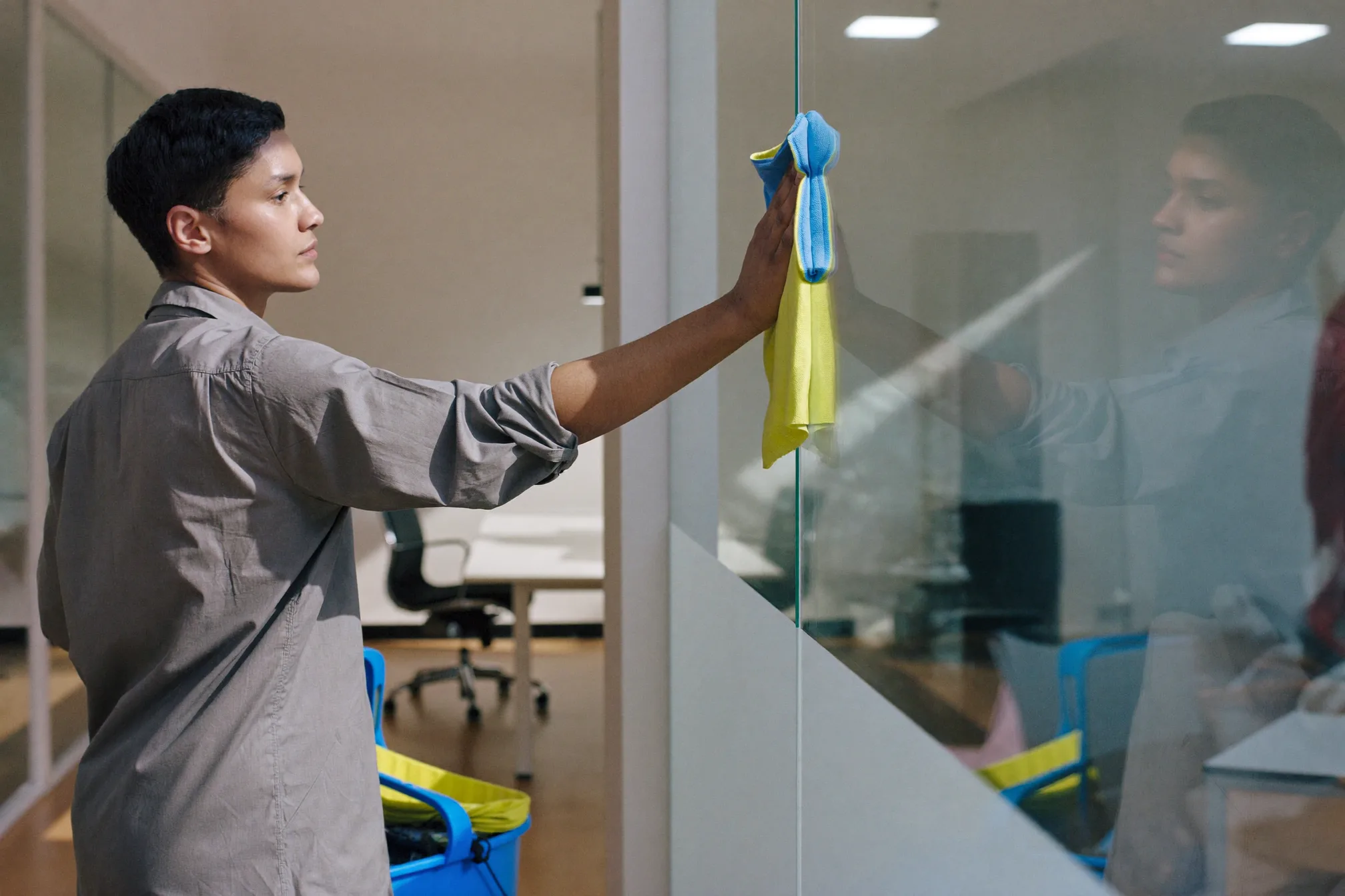 A cleaner wiping down a glass office partition in a bright modern office